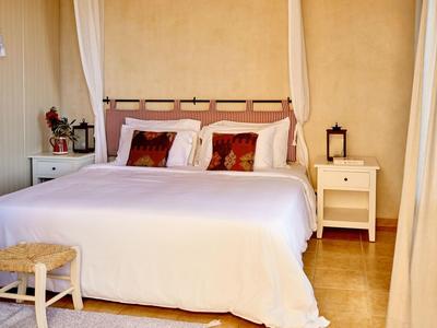 Camera luminosa con letto bianco, comodini e sgabello.