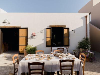 Stół jadalny nakryty naczyniami i drewnianymi krzesłami przed białym domem z otwartymi okiennicami.