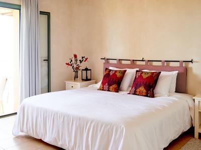 Camera luminosa con grande letto, biancheria bianca e cuscini colorati vicino al balcone.