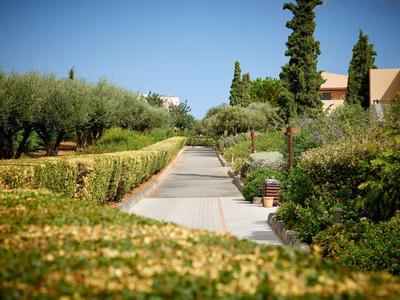 Un viale soleggiato con siepi curate e alberi in una struttura alberghiera.