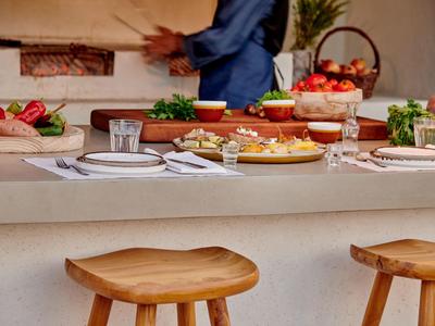Un bancone per la colazione con sgabelli in legno e tavola apparecchiata, con un cuoco sfocato sullo sfondo.