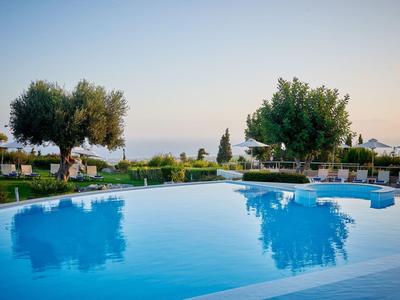 Heldere blauwe zwembad omringd door ligstoelen en groene bomen onder een heldere lucht.
