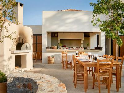 Strefa zewnętrzna hotelu z drewnianymi krzesłami i stołami oraz wbudowanym kamiennym grillem.