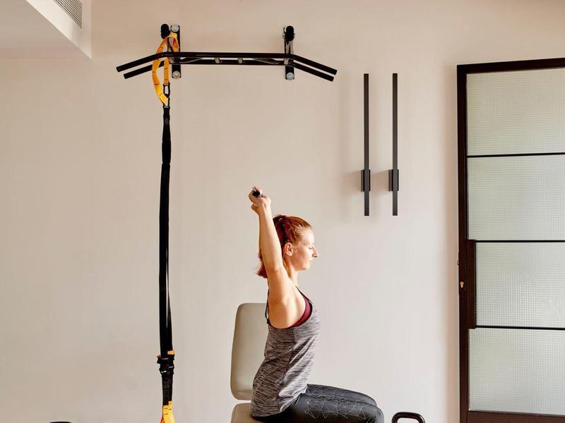 Donna si allena con bande TRX in una sala fitness luminosa con kettlebell.