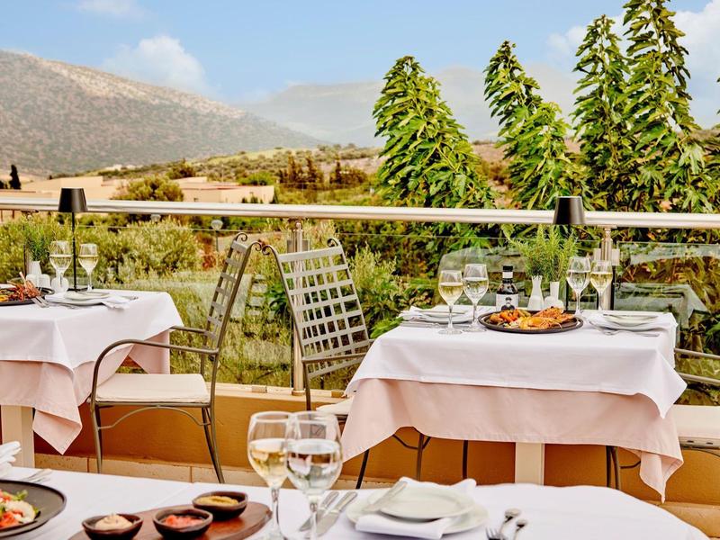 Terrazza con tavoli apparecchiati, vista su montagne e alberi verdi sullo sfondo.