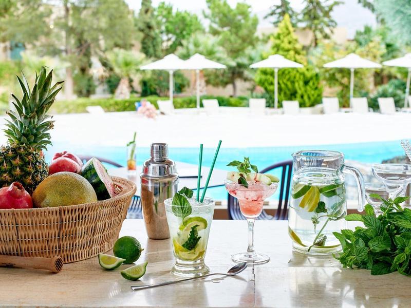 Scena estiva al bar con frutta fresca, cocktail e piscina sullo sfondo.