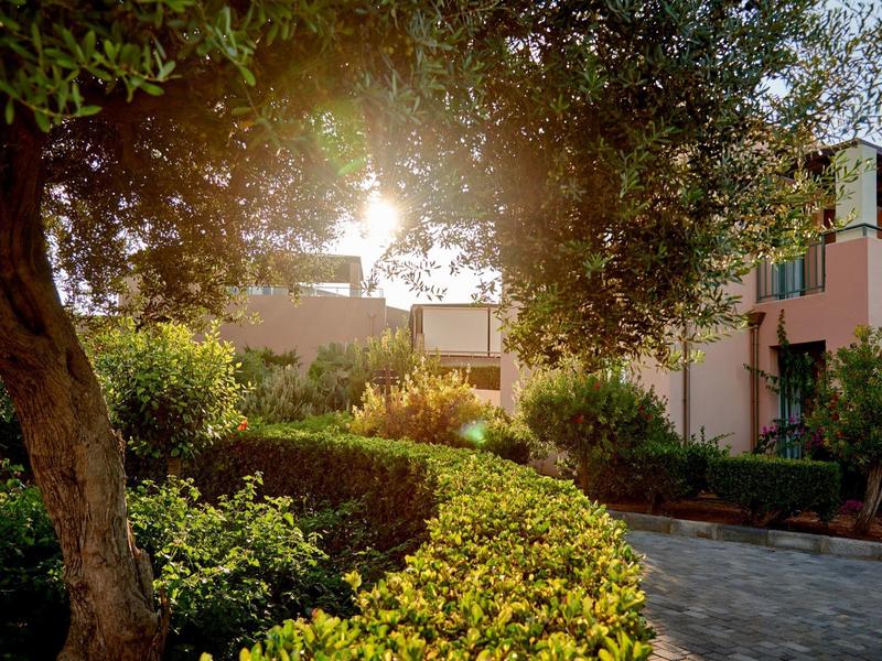 Camera luminosa con grande letto, biancheria bianca e cuscini colorati vicino al balcone.