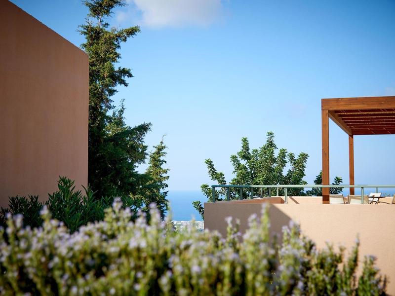 Area dell'hotel moderna con terrazza, piante e vista sul mare sotto un cielo blu.