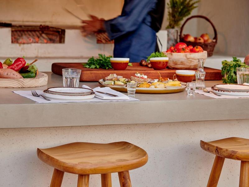 Un bancone per la colazione con sgabelli in legno e tavola apparecchiata, con un cuoco sfocato sullo sfondo.
