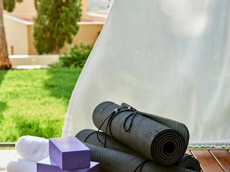 Due tappetini da yoga neri arrotolati e tre blocchi viola su un pavimento in legno davanti a una tenda bianca.