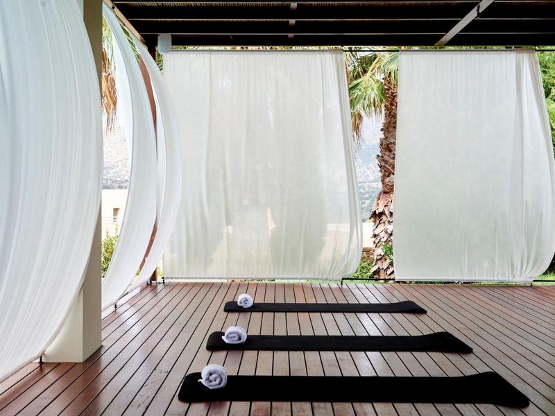 Tappetini per meditazione davanti a tende bianche su una terrazza in legno con vista sulle palme.