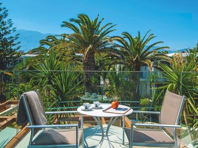 Balkon mit Tisch und Stühlen vor Palmen und Bergen bei klarem Himmel.