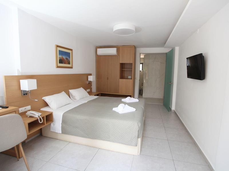 Lichte, moderne hotelkamer met tweepersoonsbed, bureau, tv en schone marmeren tegels.