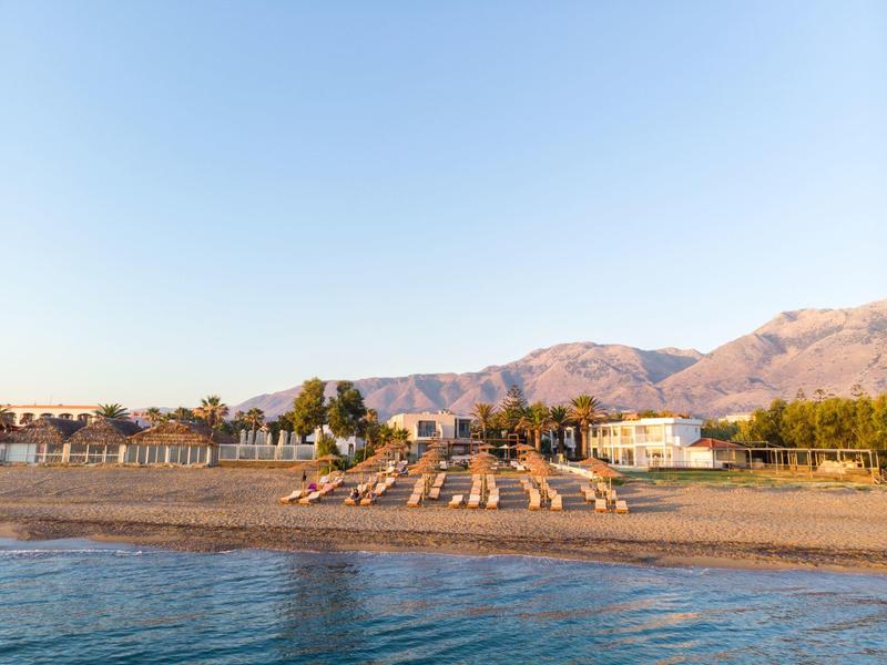 Zonnig strand met ligstoelen en bergen op de achtergrond.