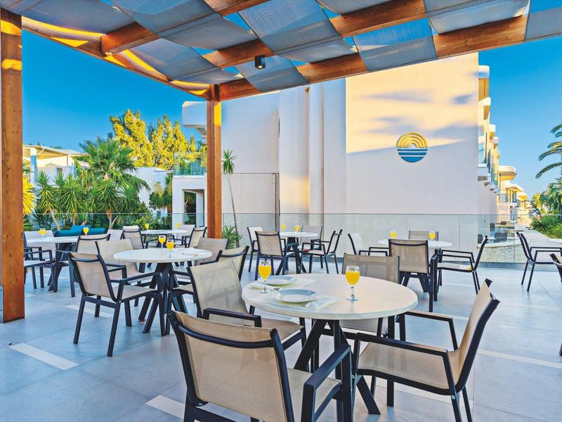 Terras met gedekte tafels en stoelen onder een houten pergola bij helder weer.