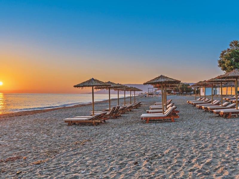 Strand met ligbedden en parasols bij zonsondergang aan zee.
