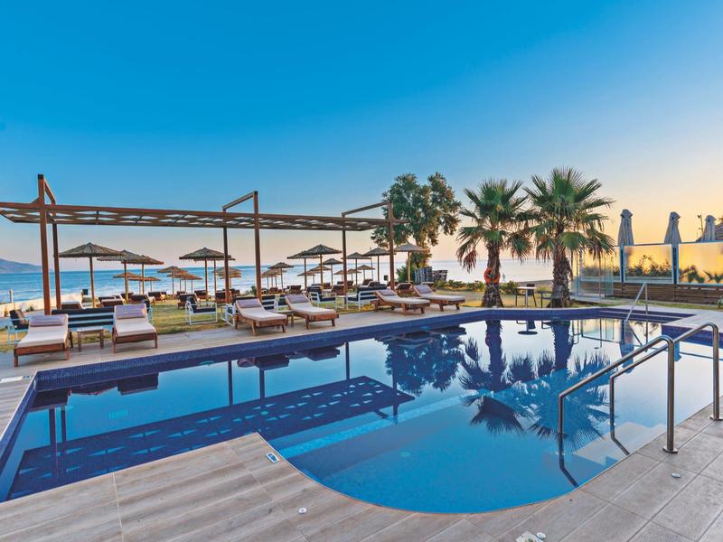 Moderne zwembaden met ligstoelen, palmbomen en uitzicht op zee bij heldere lucht.