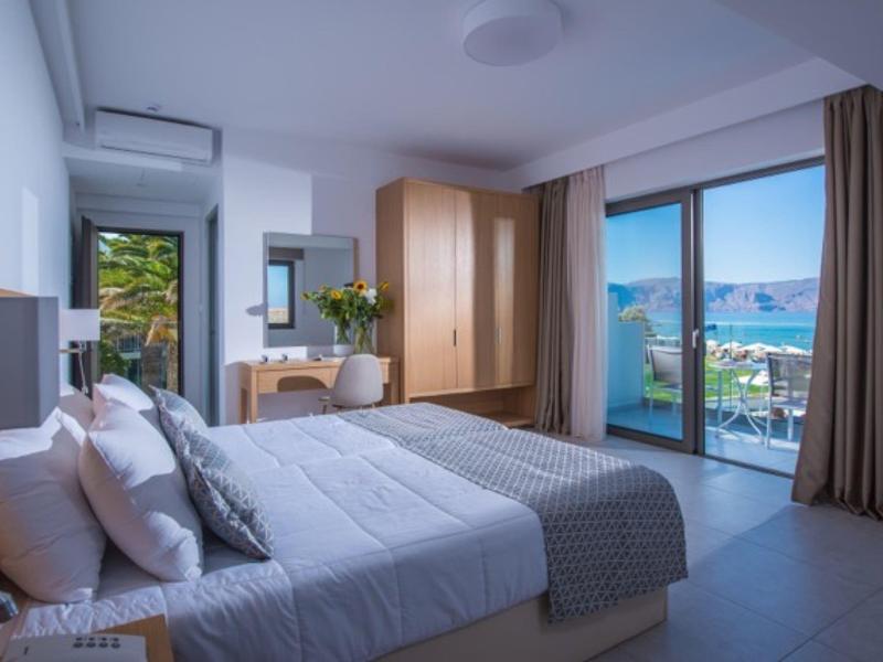 Moderne hotelkamer met tweepersoonsbed, houten kast, bureau en balkon met zeezicht.