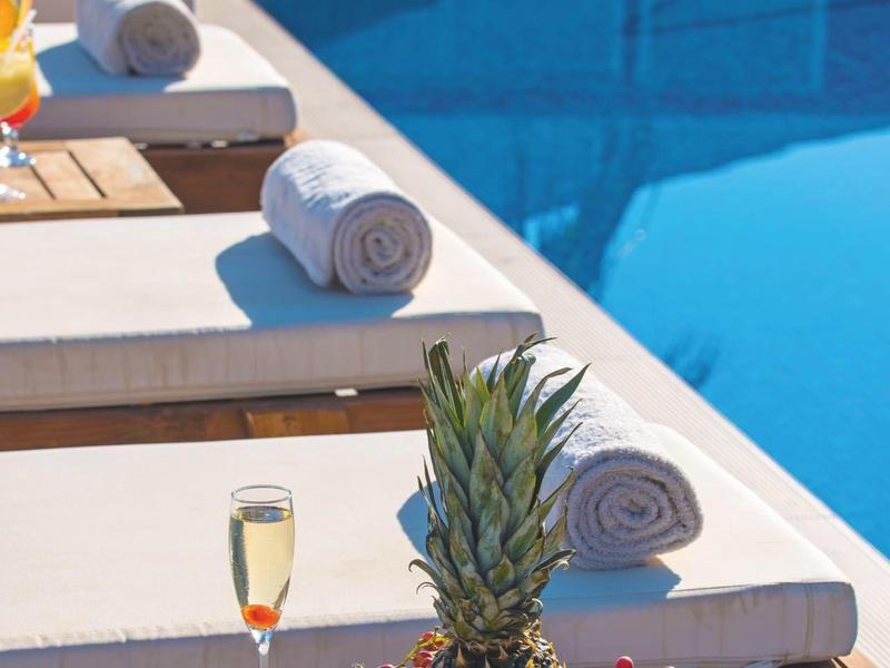 Ligbedden bij zwembad met handdoeken, fruitmand met ananas en drankje.