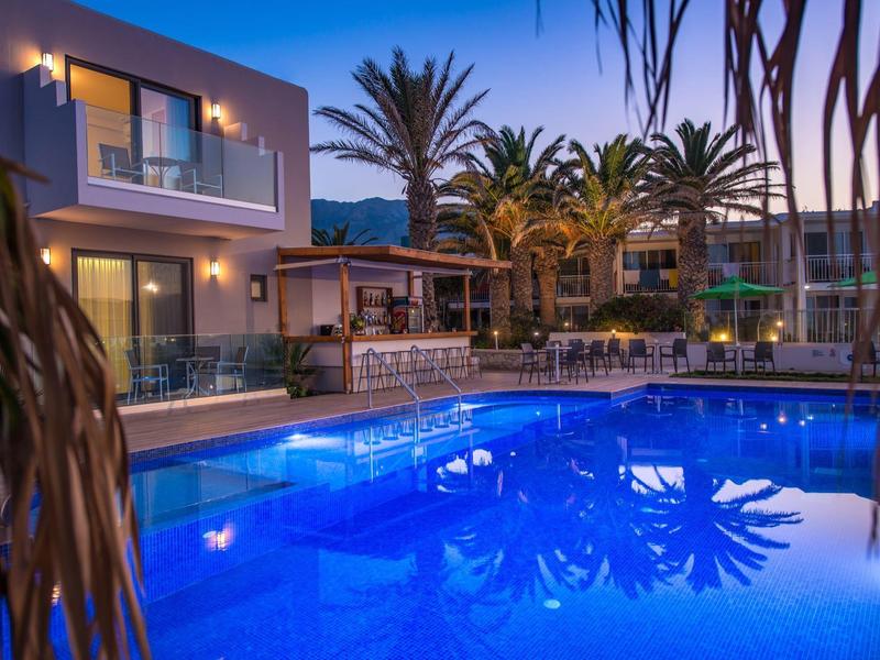 Moderne accommodatie met verlicht zwembad en palmbomen bij zonsondergang.