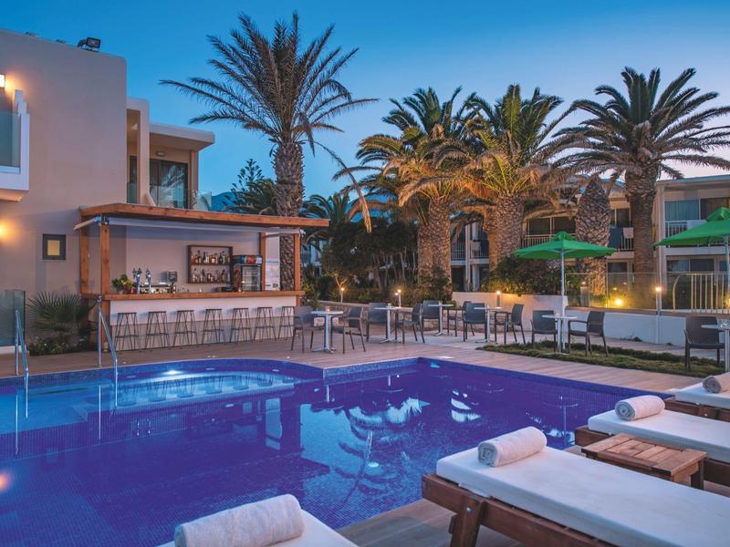 Verlichte zwembad met ligstoelen en bar in tropische hotelomgeving bij schemering.