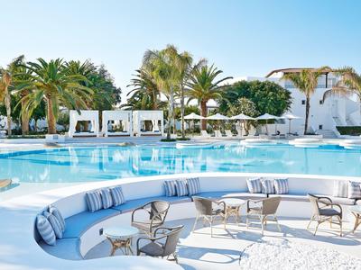 Round seating area with cushions in front of large pool and palm trees at a hotel resort.