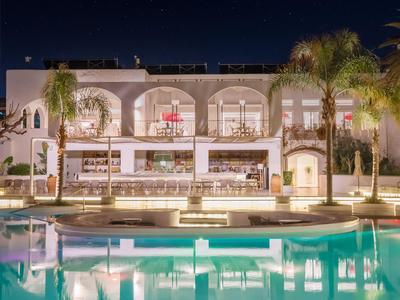 Evening view of a hotel with lit pool and palm trees in the foreground