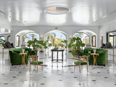 Elegantní hotelová lobby s zelenými křesly, barovými židlemi a velkými okny