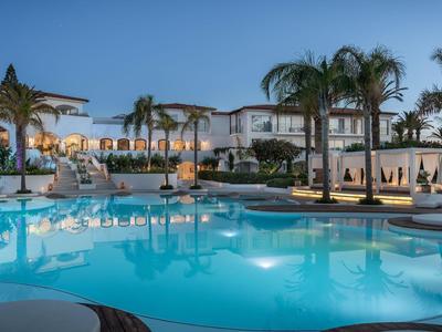 Luxury hotel with illuminated swimming pool and palm trees at night.