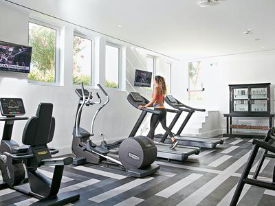 Well-lit gym with modern equipment and a woman on the treadmill.