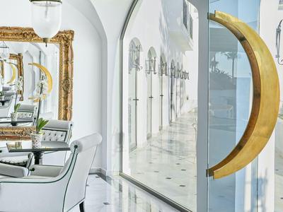 Elegantní hotelová hala s bílým interiérem, velkými zrcadly a zlatou dekorací ve tvaru měsíce.