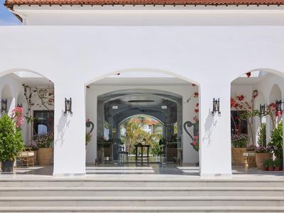 Bílá budova s oblouky a nádvořím, viditelné nábytek a rostliny.