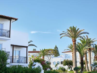 Bílé hotelové budovy s balkony a palmami pod jasně modrou oblohou