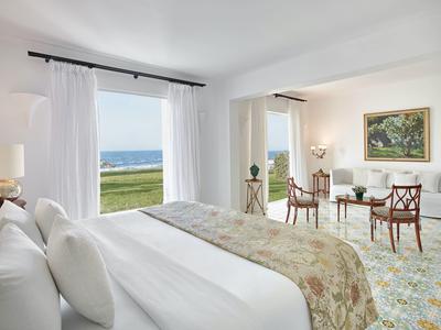 Světý pokoj hotelu s velkou postelí a výhledem na moře přes dvě okna.