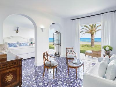 Světý hotelový pokoj s výhledem na moře, bílým zařízením a modře vzorovanou podlahou.