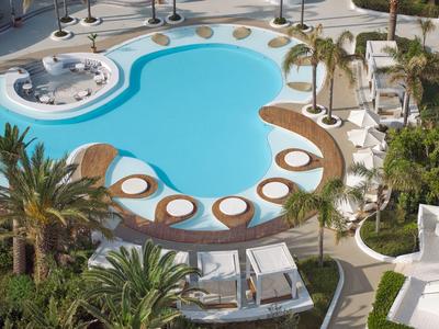 Curved-shaped pool area surrounded by lounge chairs and palm trees.