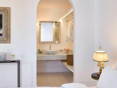 Světle moderní hotelový pokoj s bílým zařízením a ozdobným zrcadlem.