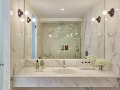 Moderní koupelna s bílým mramorem, umyvadlem a osvětleným zrcadlem.