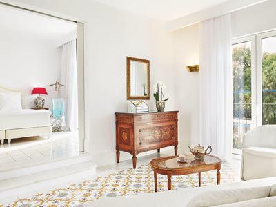 Světý obývací pokoj s bílým nábytkem, dřevěnými kusy a velkými okny s výhledem na zeleň.