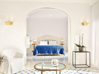 Světlý hotelový pokoj s bílým nábytkem, modrou postelí a rostlinami v moderním prostoru.