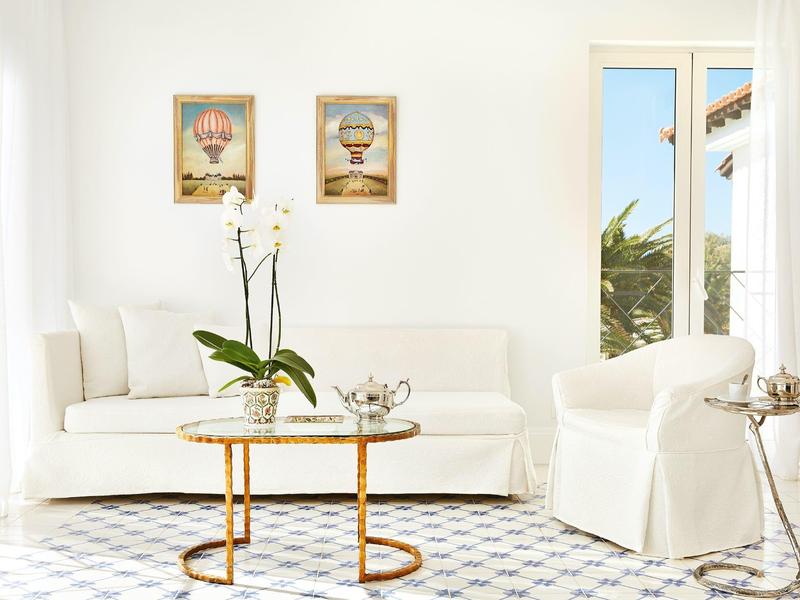 Světý obývací pokoj s bílou pohovkou, křesly a kulatým skleněným stolem s rostlinami a čajovým servisem