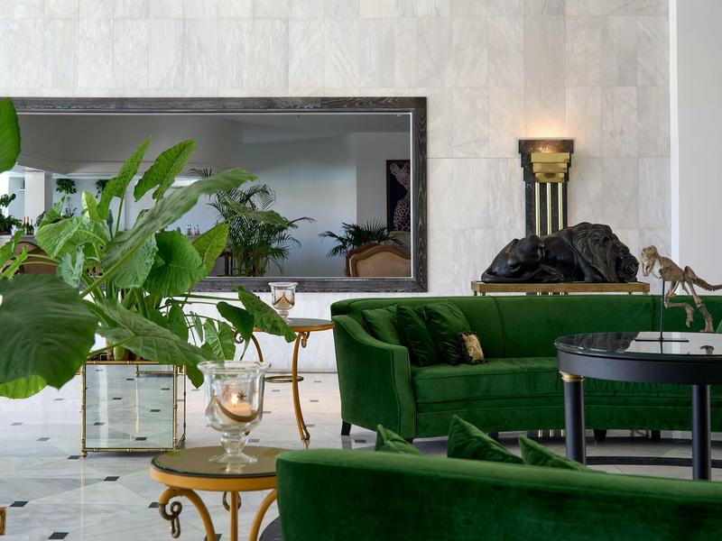 Elegantní obývací pokoj se zelenou sametovou pohovkou, černým a zlatým nábytkem a velkými rostlinami.