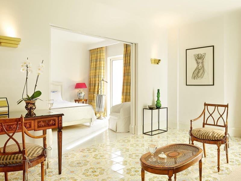 Světý obývací pokoj s elegantním nábytkem, dřevěnými židlemi a malým stolkem v stylovém hotelovém pokoji.