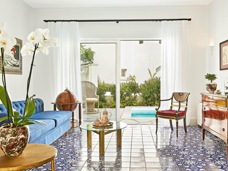 Světlý obývací pokoj s modrou pohovkou, skleněnými posuvnými dveřmi do zahrady s bazénem, barevná dlažba.