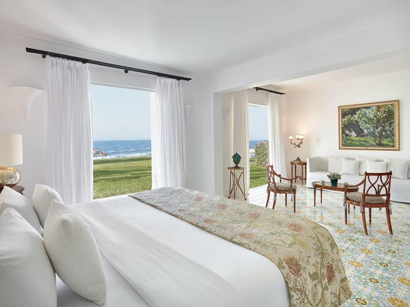 Světý pokoj hotelu s velkou postelí a výhledem na moře přes dvě okna.