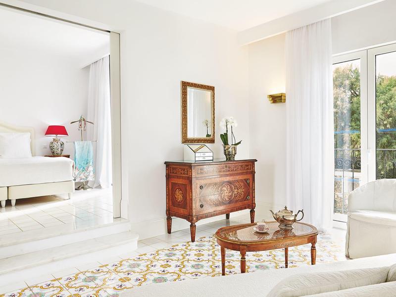 Světý obývací pokoj s bílým nábytkem, dřevěnými kusy a velkými okny s výhledem na zeleň.