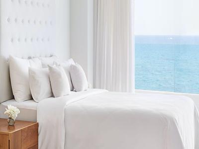 Camera luminosa con letto bianco e vista mare attraverso una grande finestra