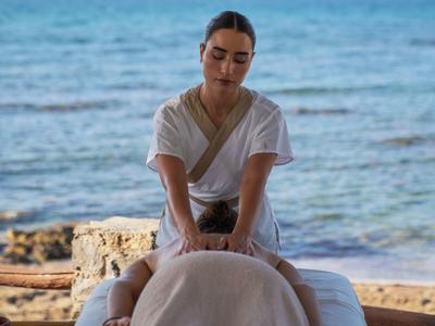 Frau in weißen Kleid erhält am Meer eine Rückenmassage auf einer Massagebank.