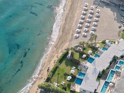 Vogelperspektive auf Strand mit Sonnenschirmen, blauem Meer, Pools und grünen Rasenflächen.