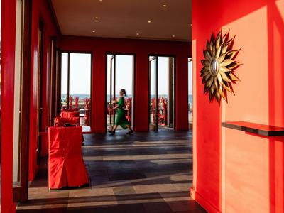 Lounge dell'hotel con pareti rosse, sedie e decorazione solare al tramonto.